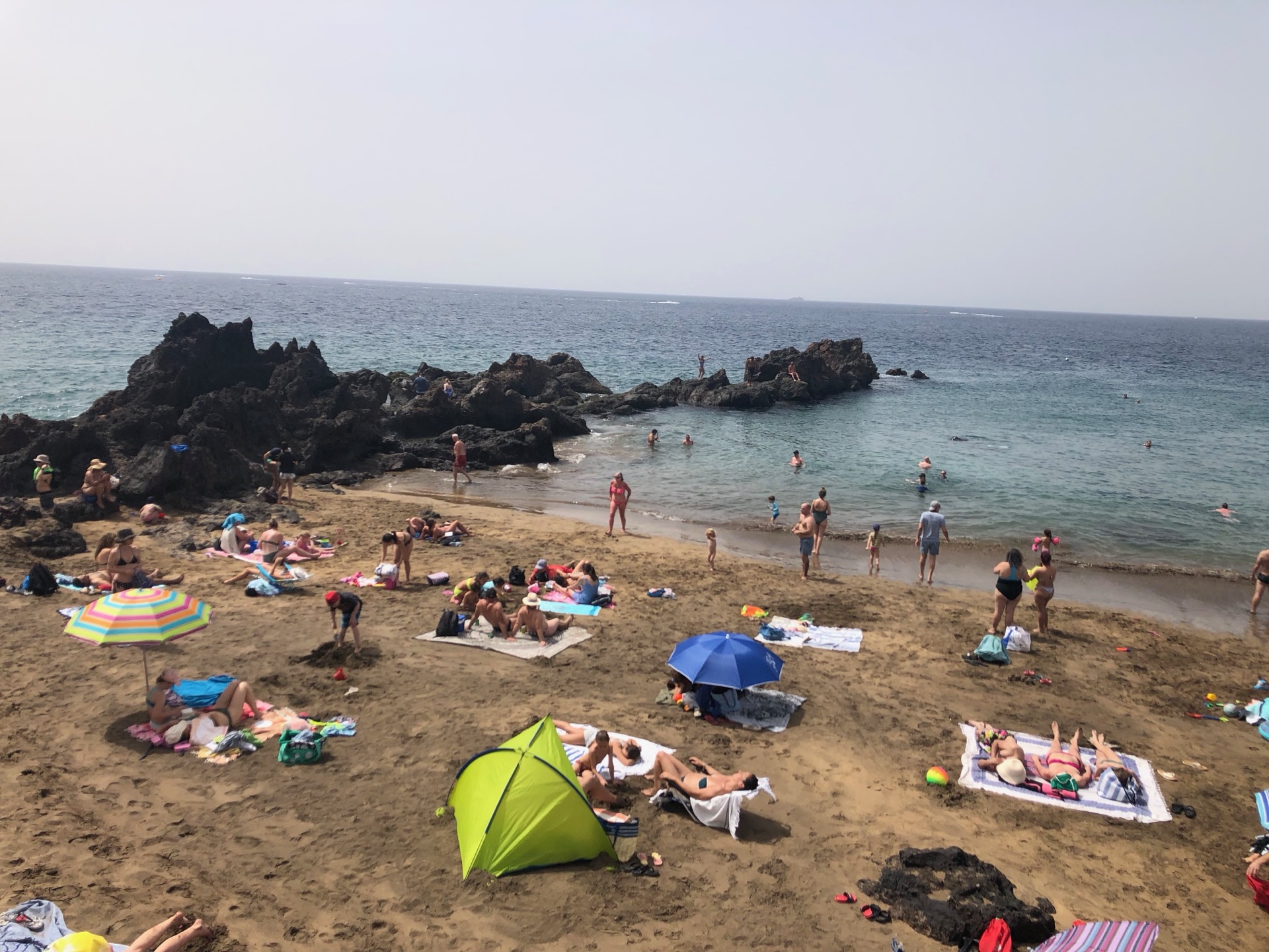 Badestrand auf Lanzarote mit Badegästen, Sonnenschirmen und schwarzen Lavafelsen im Sommer
