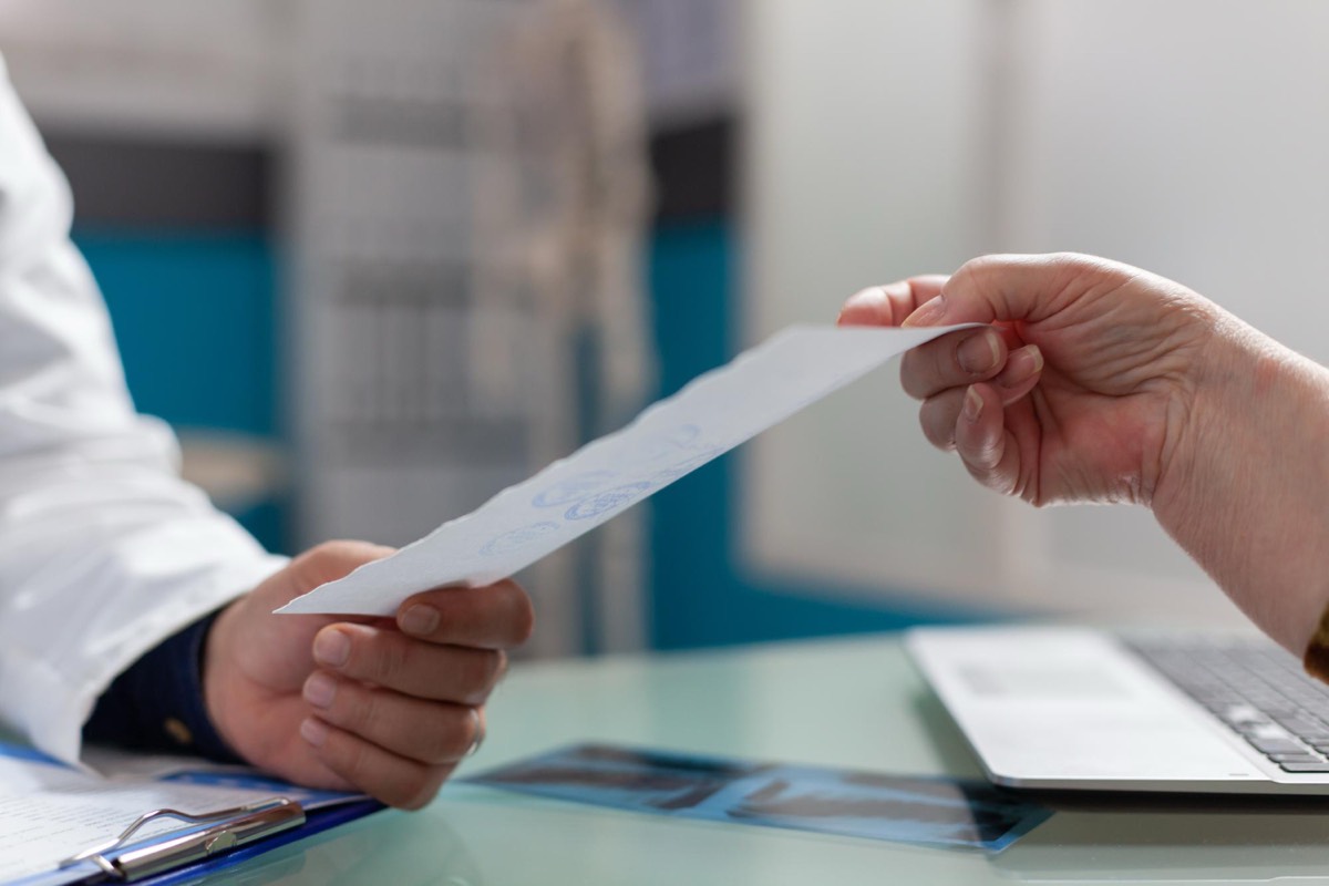 Arzt übergibt Rezept an Patientin in der Arztpraxis