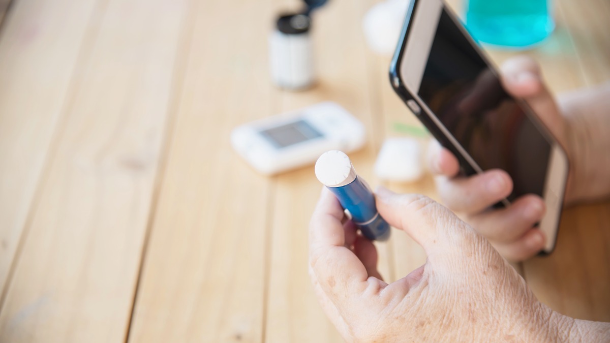 Ältere Person misst Blutzucker am Strand – Diabetes im Urlaub auf Lanzarote
