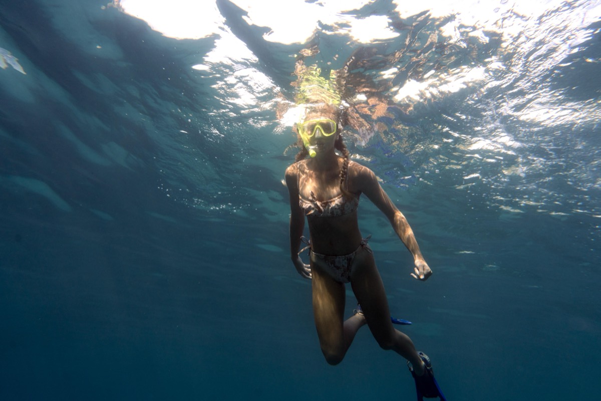 Schnorchlerin mit gelber Tauchermaske und blauen Flossen taucht im dunkelblauen Atlantik knapp unter der Wasseroberfläche