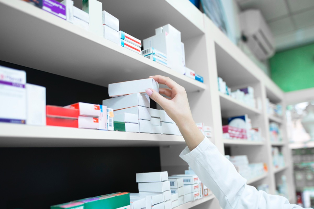 Apothekerin greift Medikamentenpackung aus gut sortiertem Apothekenregal