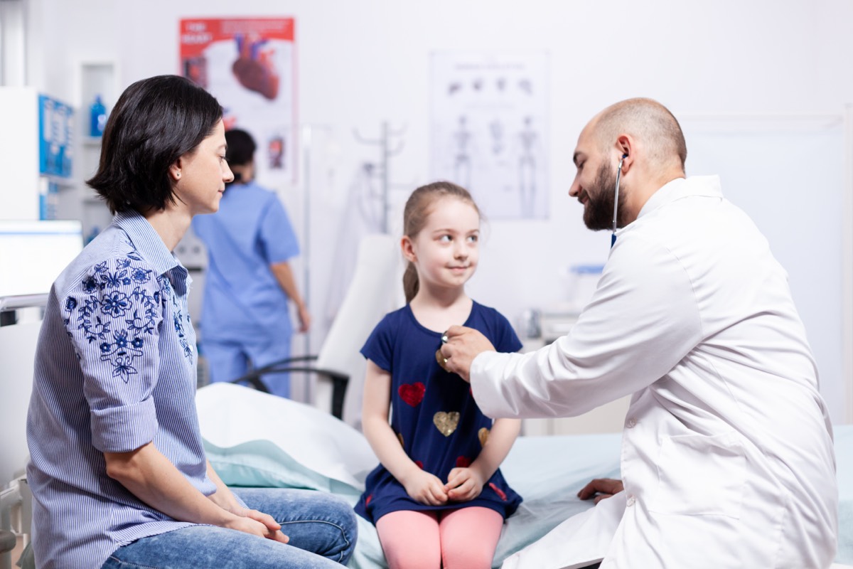 Ärztin untersucht ein Kleinkind mit Stethoskop in einer hellen Kinderarztpraxis