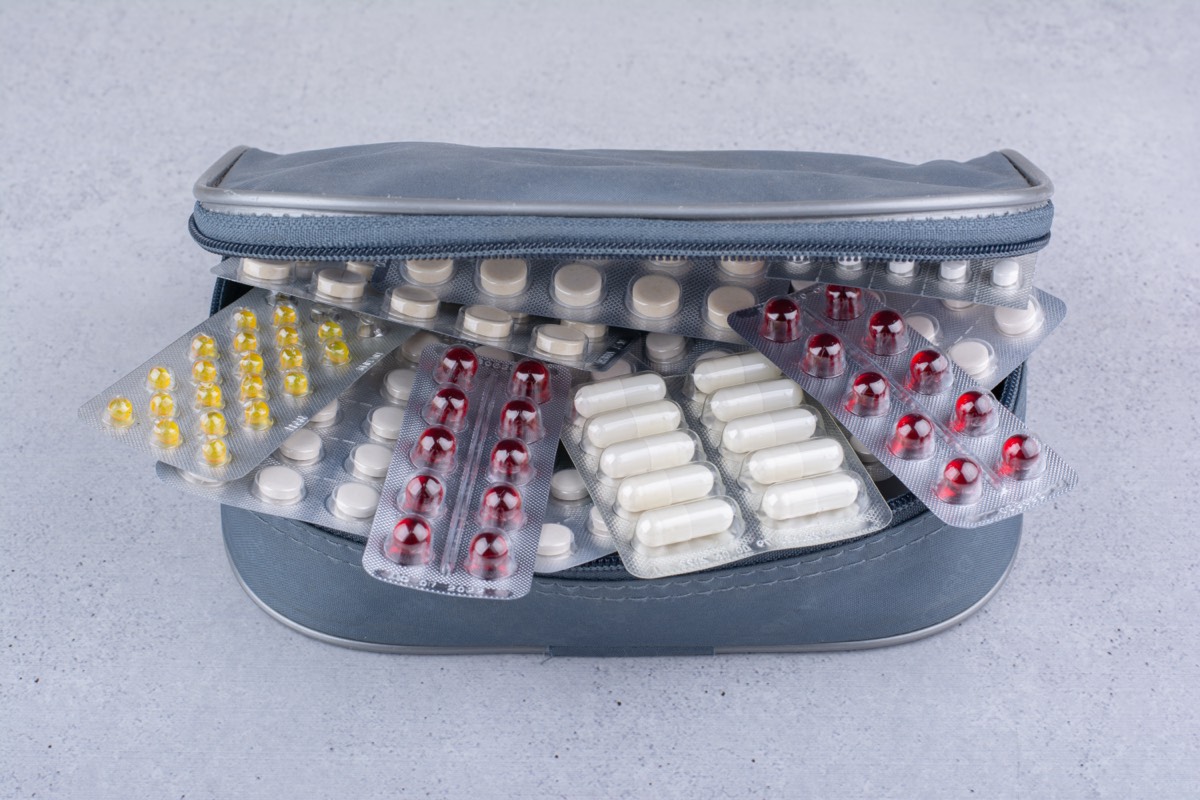Geöffnete graue Reiseapotheken-Tasche gefüllt mit bunten Blisterpackungen – gelbe, rote und weiße Kapseln und Tabletten auf Marmor