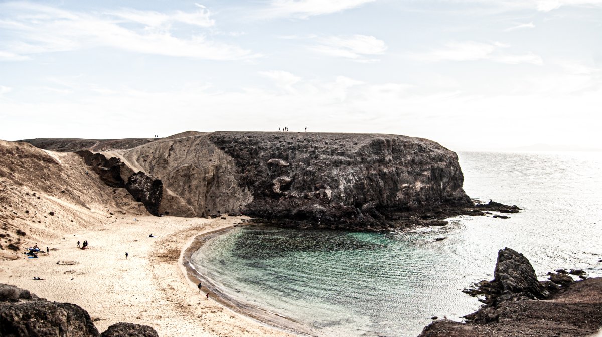 Blick auf die Küstenpromenade von Playa Blanca auf Lanzarote mit türkisblauem Wasser, weißen Gebäuden und dem Hafen im Hintergrund