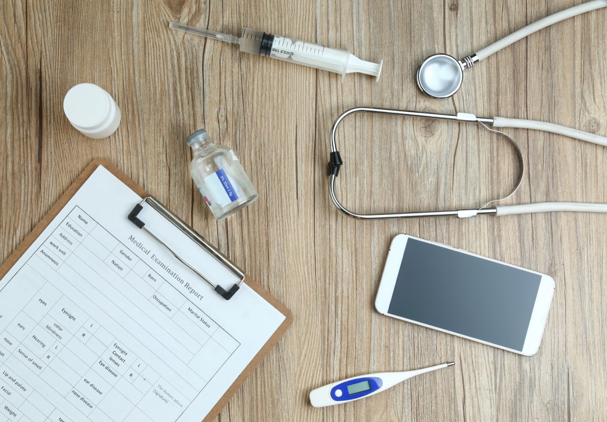 Draufsicht auf medizinischen Befundbogen mit Stethoskop und Thermometer auf Holztisch – Krankenversicherung im Urlaub